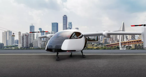 A flying vehicle on a tarmac with a city skyline behind it. 