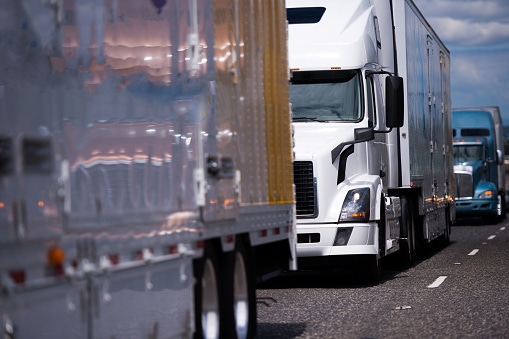 Convoy of big rigs customized semi trucks in different colors and different styles and models with semi trailers driving side Convoy of big rigs customized semi trucks in different colors and different styles and models with semi trailers driving side