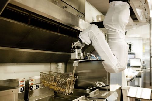 Robot arm operating a deep fat fryer in a commercial kitchen