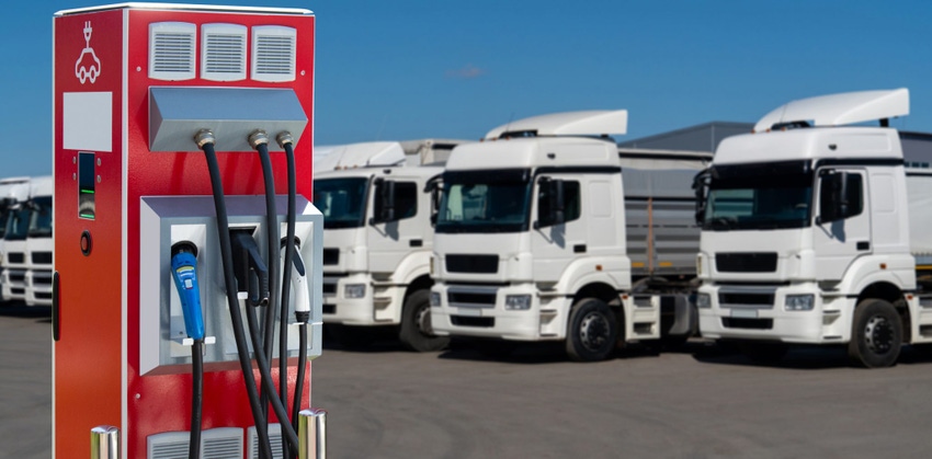 Image shows electric vehicles charging station with trucks in the background.