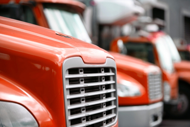 Image shows a middle sized rigs semi trucks standing in row in warehouse dock for loading cargo