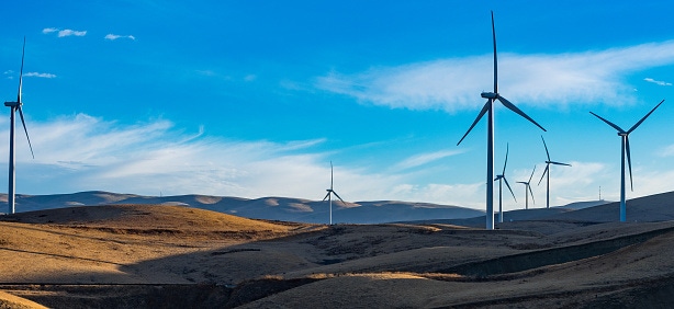 Image shows giant wind turbines overlooking a hillside..
