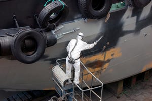 A dockyard worker removes rust from a ship hull