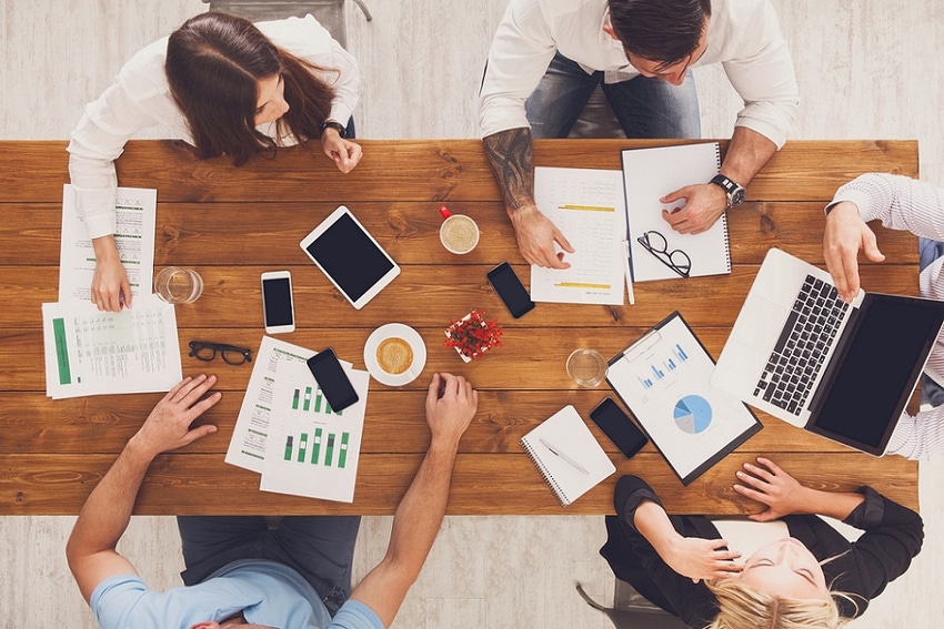 Group of busy business people working in office, top view of wooden table with mobile phones, laptop, tablet and documents pa