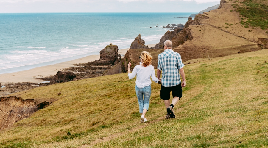 man and woman walking hand in hand along coastline overlooking beach in Cornwall