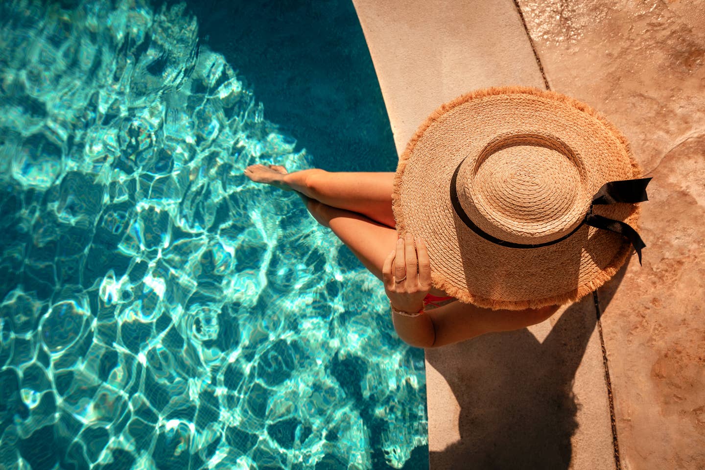 Frau, die am Poolrand sitzt und die Beine ins Wasser hält.