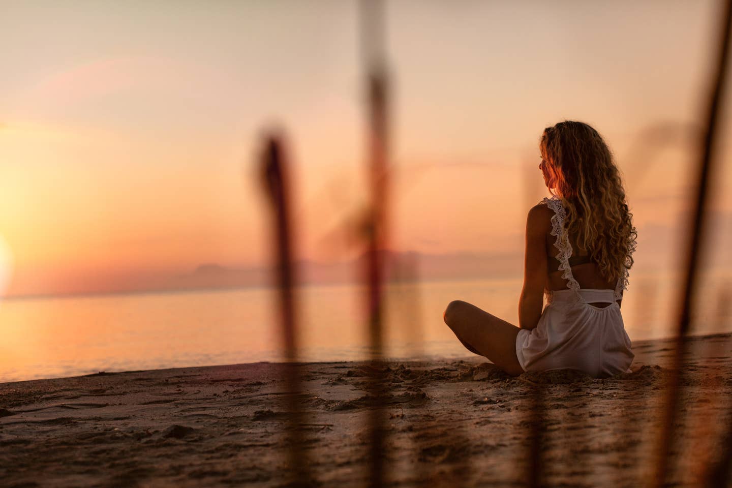 Frau, die in der Abendsonne am Sandstrand sitzt und aufs Meer hinausblickt. Frau, die in der Abendsonne am Sandstrand sitzt und aufs Meer hinausblickt.