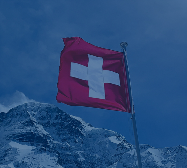 Man sieht eine Schweizer Flagge sowie Berge im Hintergrund.