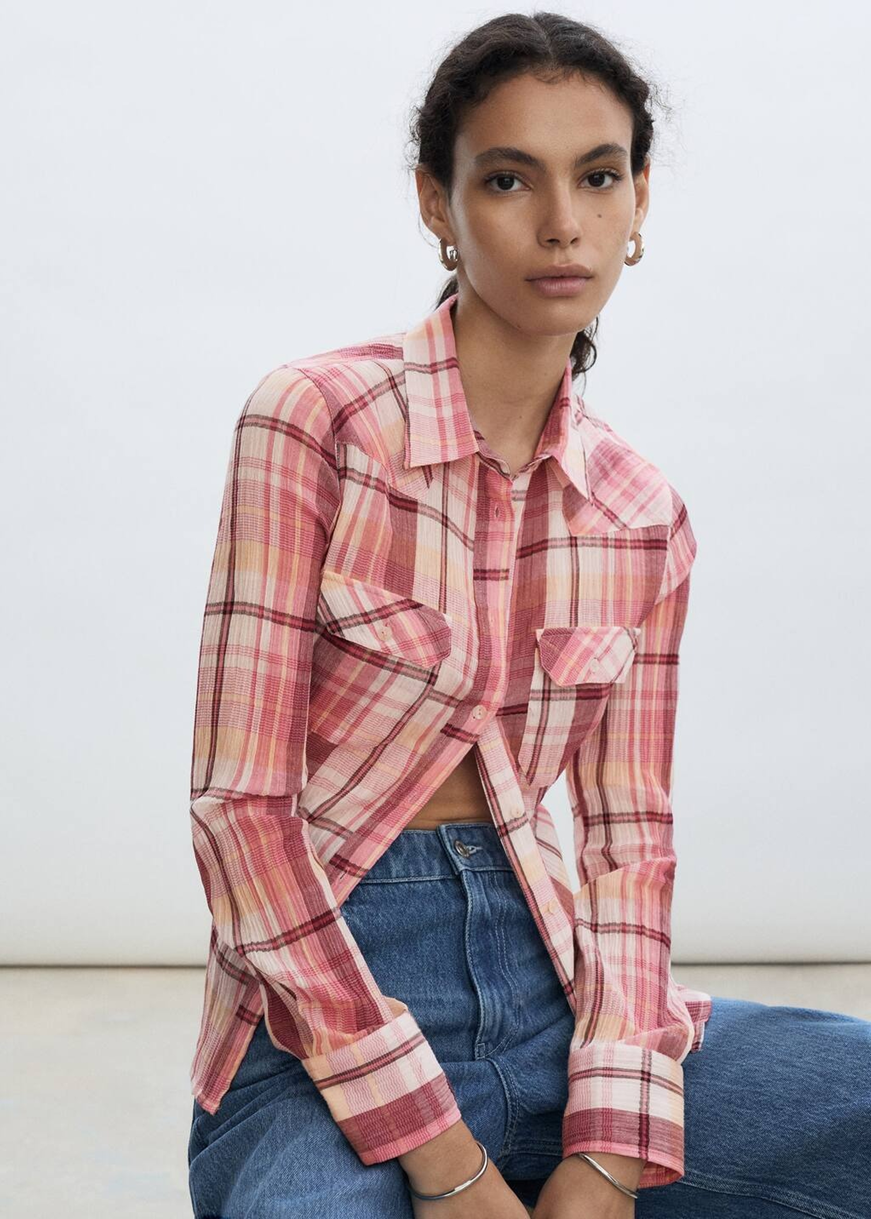 Femme assise portant un look décontracté avec un chemisier imprimé et un jean.