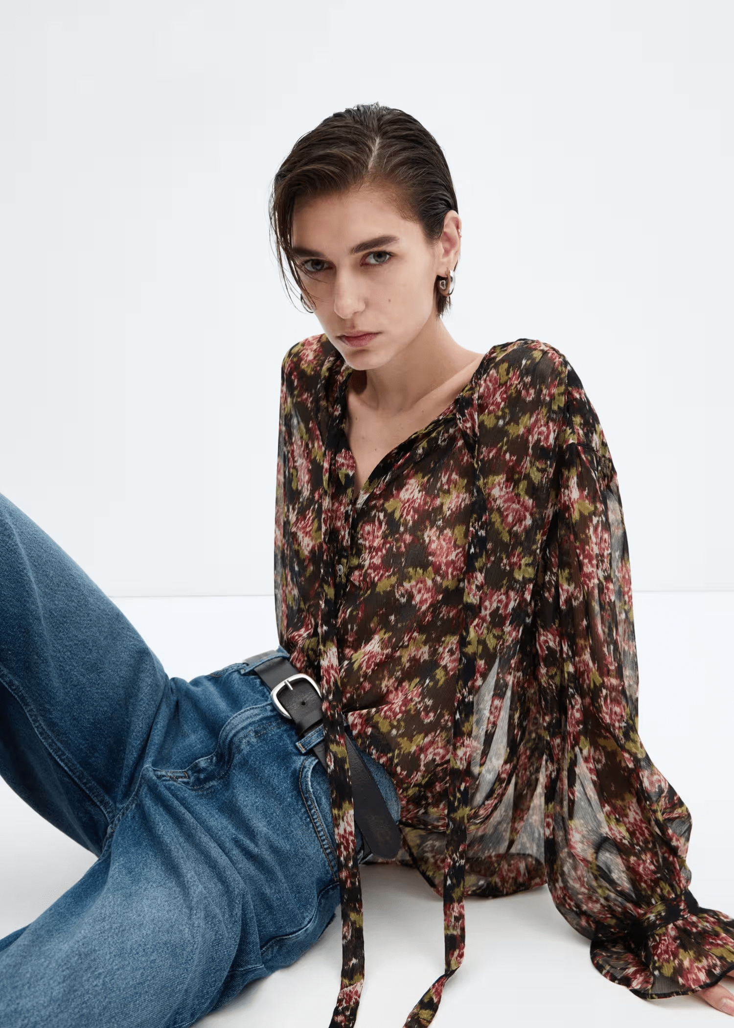Seated woman wearing a casual look with a printed blouse and jeans.