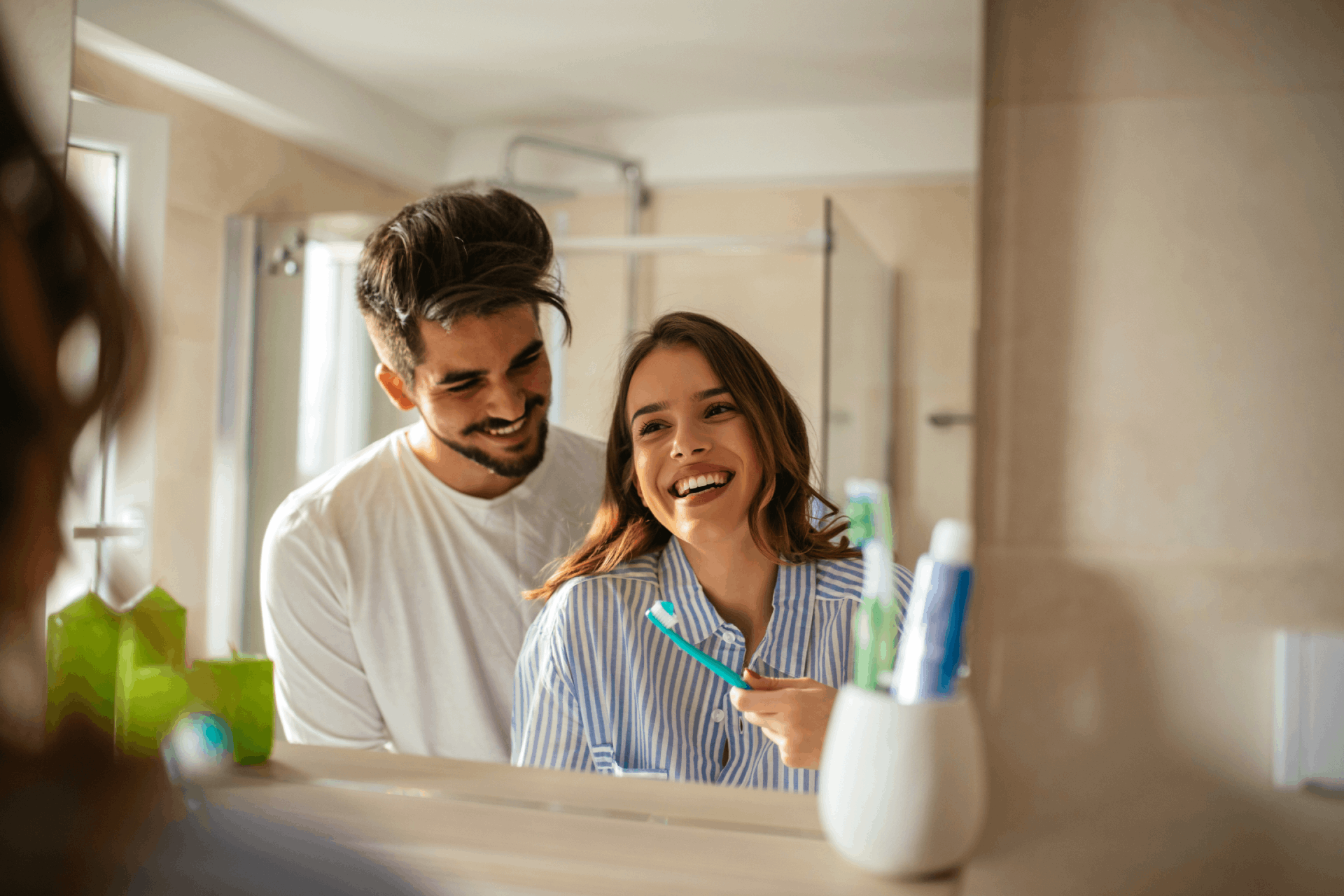 Hombre y mujer con cepillo de dientes sonriendo frente al espejo