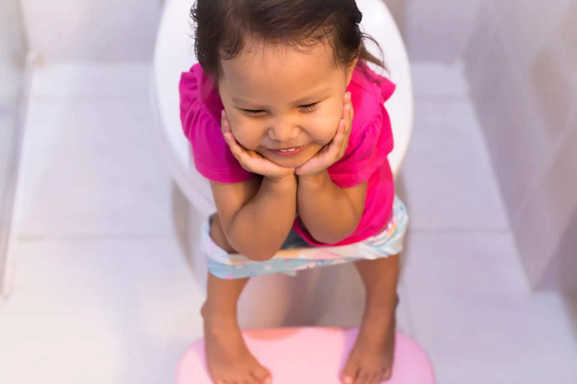Niña con vestido de color rosa sentada sobre una taza de baño