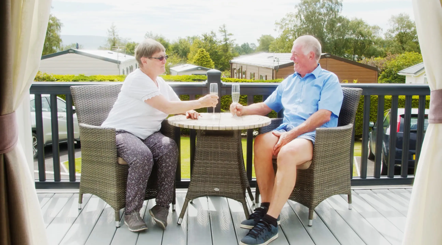 Couple sitting on their holiday home decking drinking champagne