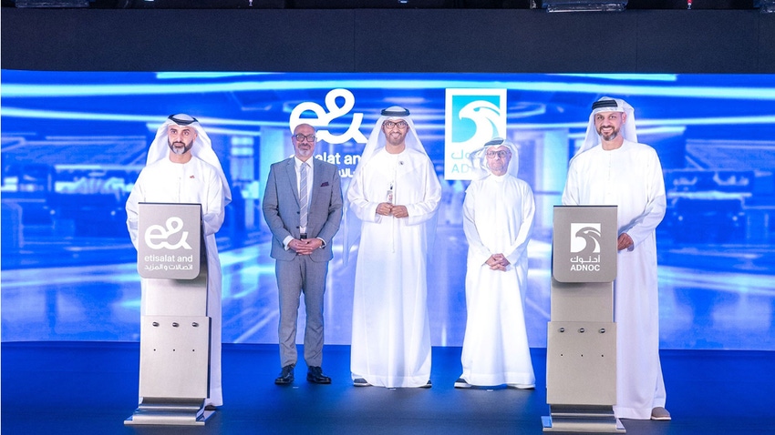 Five e& and ADNOC leaders (names unknown) standing in a formation with a blue background and the two company logos
