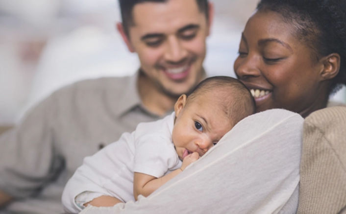Happy parents smiling while holding their newborn baby in a white blanket at home