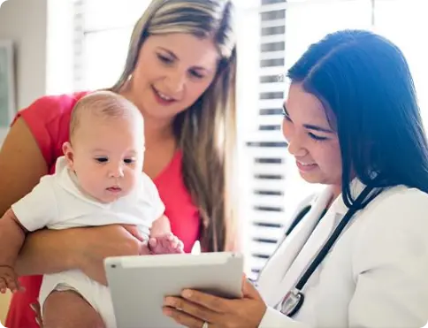 Healthcare provider with stethoscope shows tablet to mother holding baby during medical consultation
