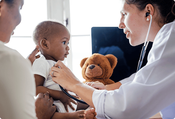 Female doctor examining infant with stethoscope while parent holds child, teddy bear visible in background