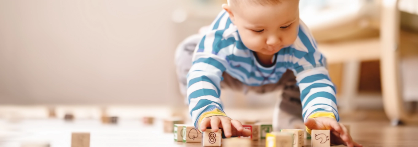 Young child in blue striped shirt playing with wooden alphabet blocks on the floor