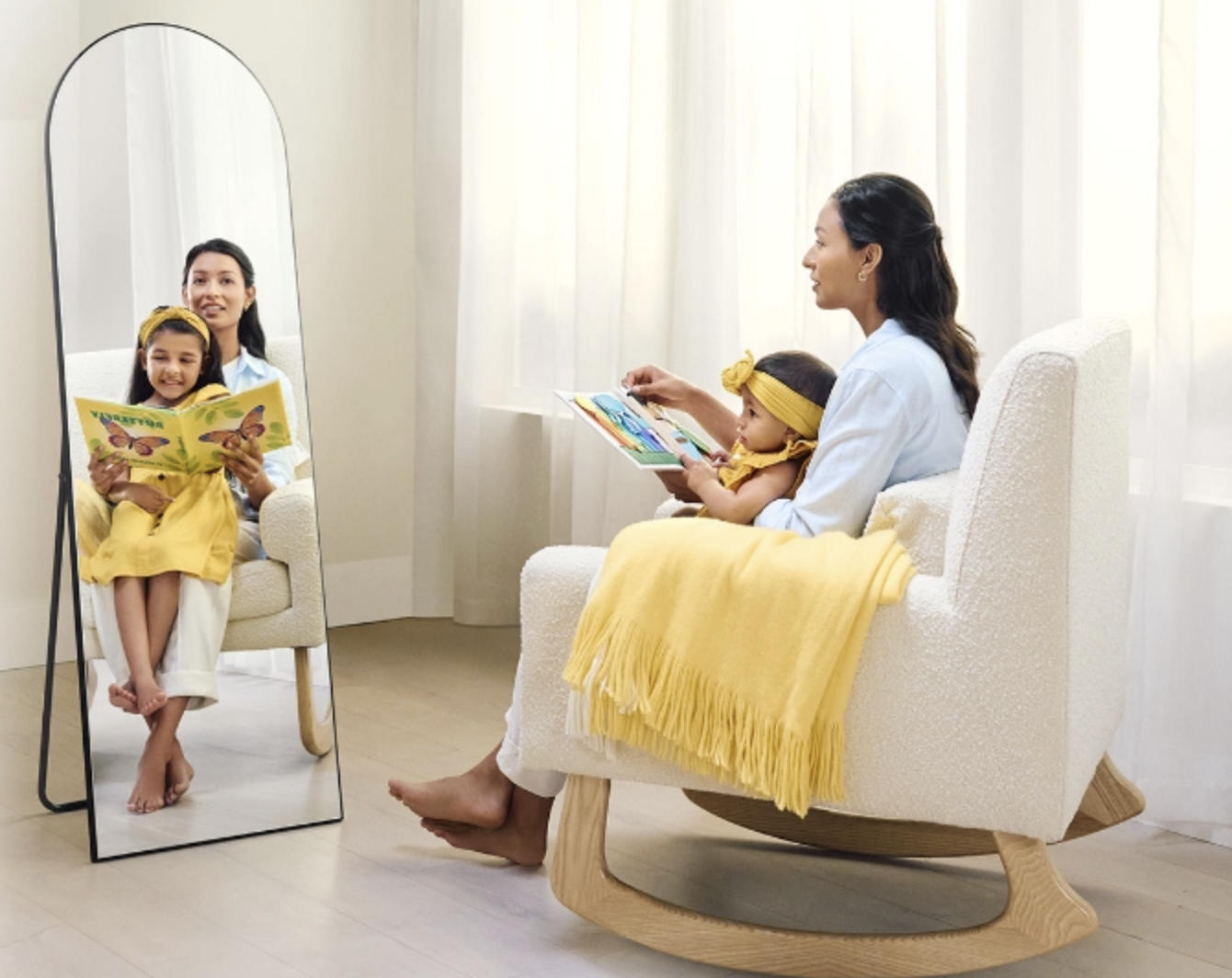 Mother and child reading together in a white rocking chair with yellow blanket, their reflection visible in a nearby mirror