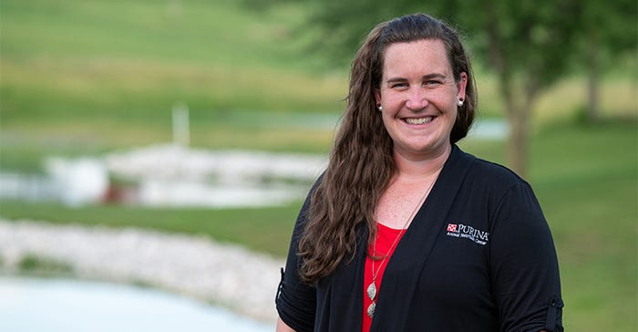 Elizabeth Backes-Belew is at the Purina Animal Nutrition Center in Gray Summit, Missouri, with green summer grass and a pond behind her. 