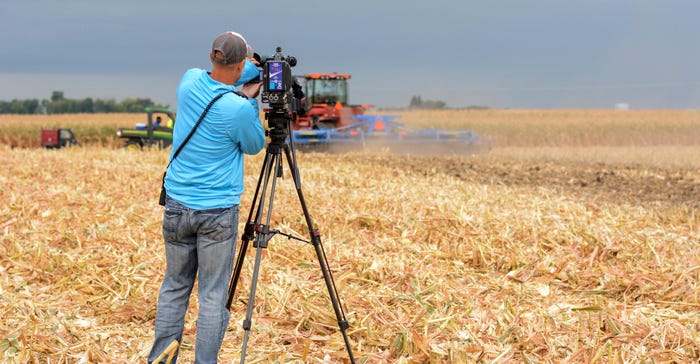 A man standing in a field with camera equipment filming a combine tractor