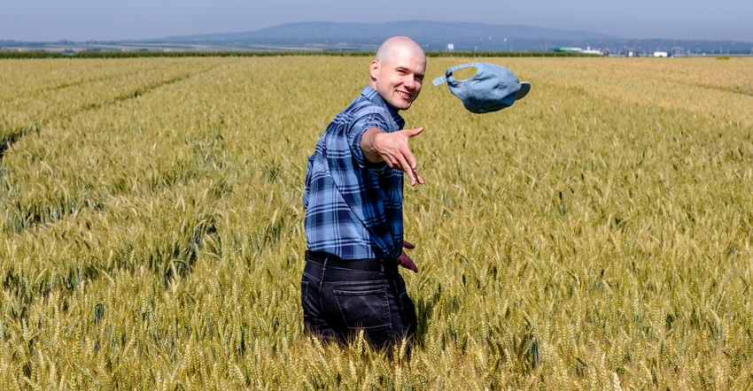 Happy farmer standing in a ripe wheat field throwing off his hat and looking at the camera