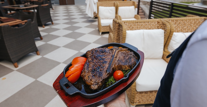 server holding plate of steak at empty restaraunt