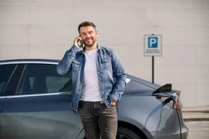 Man leaning against car on the phone while it charges Man leaning against car on the phone while it charges