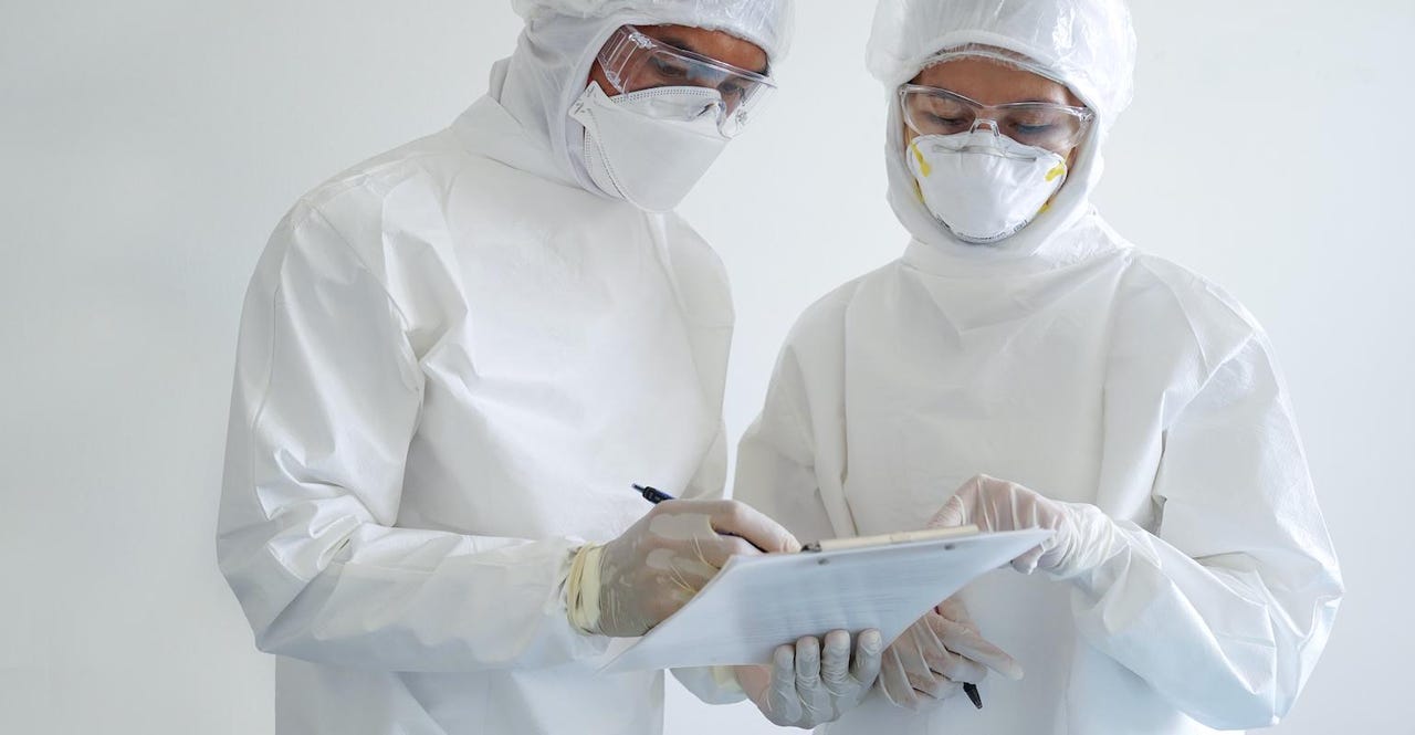 two-healthcare-workers-in-hazmat-suits-examine-clipboard.jpg two-healthcare-workers-in-hazmat-suits-examine-clipboard.jpg