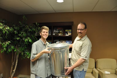 Departing Waste Age editor Stephen Ursery (left) hands off the sacred trash can to managing editor Steven Averett.