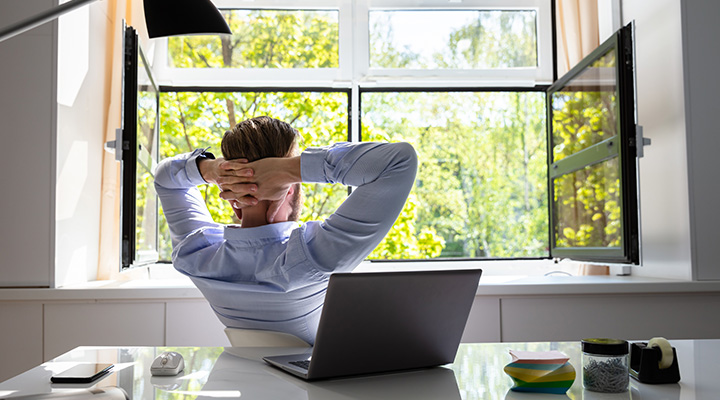 Mężczyzna odchyla się przy biurku i patrzy przez okno