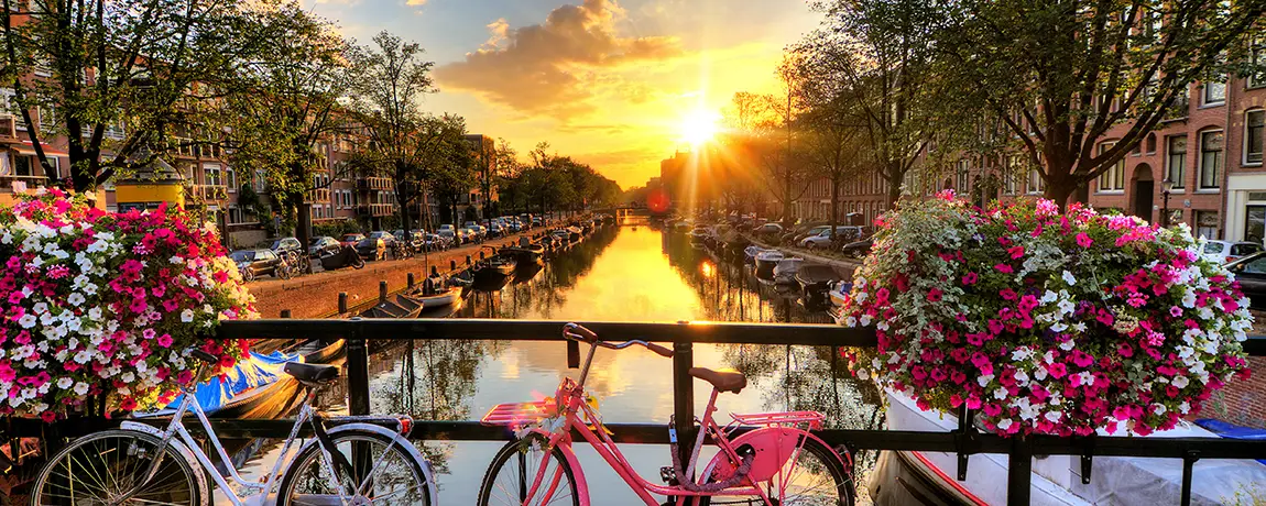 sunrise-over-Amsterdam-the-Netherlands-with-flowers-and-bicycles-on-the-bridge.webp