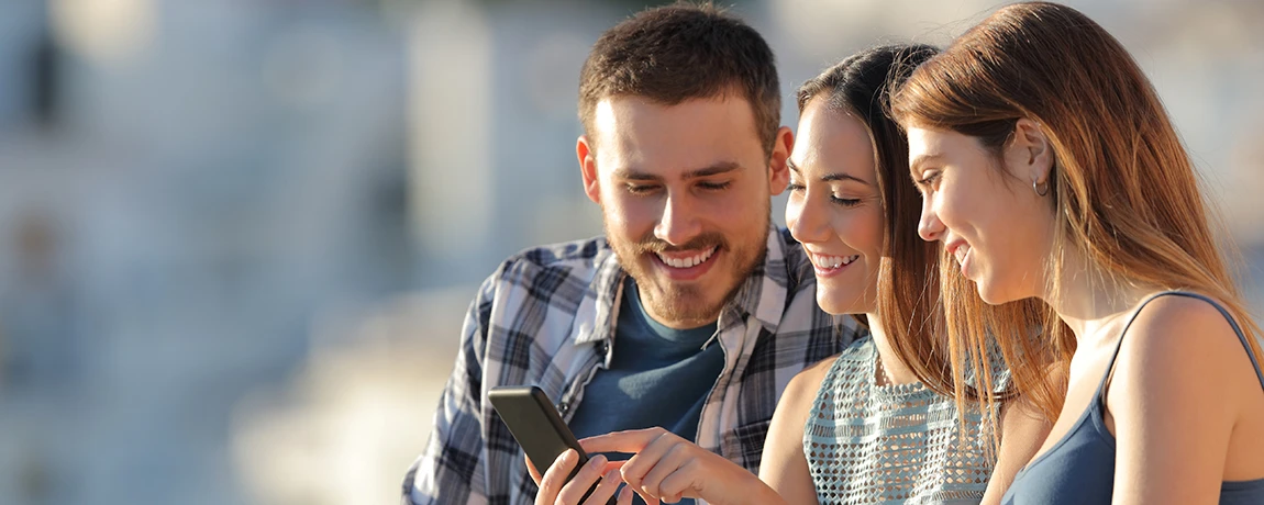 two smiling women and male looking at a phone.webp