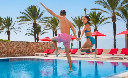 Two people are jumping into a swimming pool on holiday