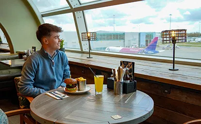 Man enjoying view of Aeroplanes while enjoying a burger and a soft drink.