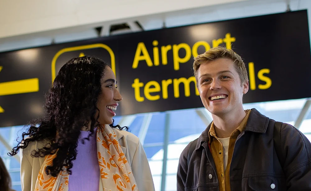 lady and man smiling under gatwick sign