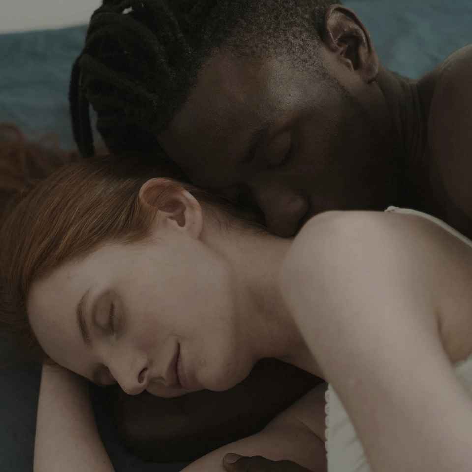 Close-up of two partners spooning while lying down in bed.