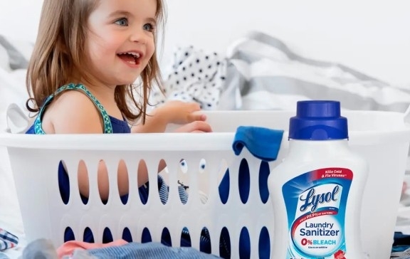 Child smiling in a white laundry basket next to a bottle of Lysol Laundry Sanitizer.