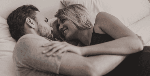 Un couple étendu au lit et se regardant dans les yeux.
