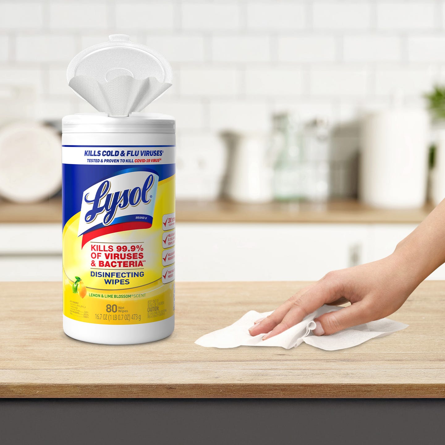 A container of Lysol disinfecting wipes on a kitchen counter with a hand using a wipe.