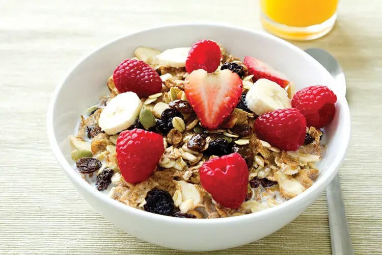 A bowl of cereal and milk with bananas raspberries strawberries and blackberries