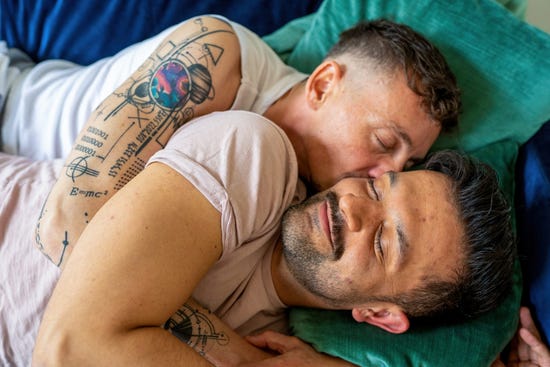 Dos hombres acostados en la cama abrazados.
