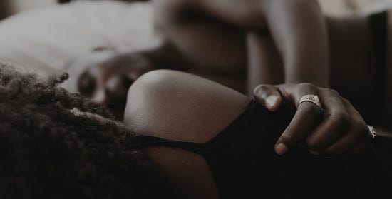 Two partners wearing black clothing clutching onto one another while lying down in bed.