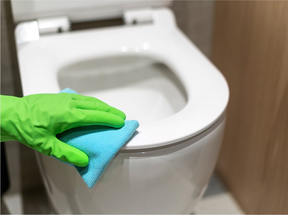 Mano limpiando el asiento del inodoro con un trapo y guante