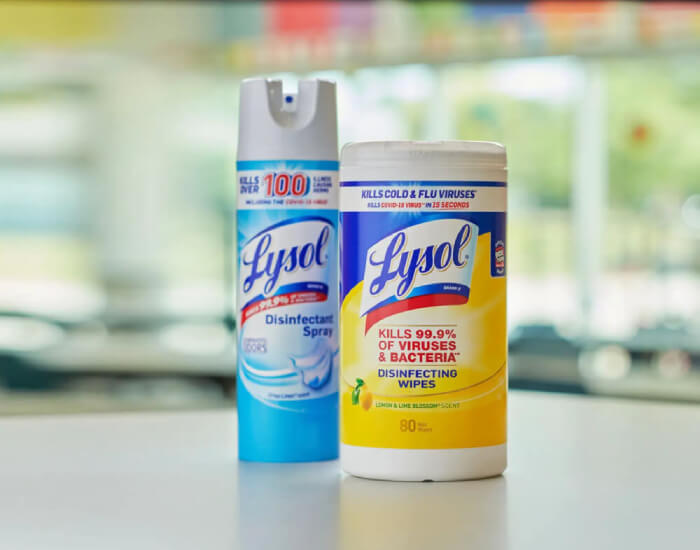 Two Lysol disinfectant products on a table: a blue spray can and a yellow wipes container.