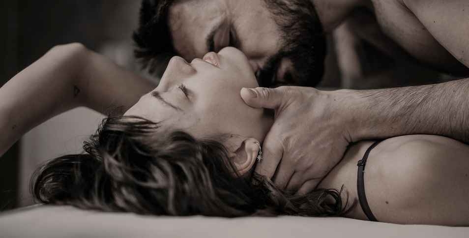 Un homme dans un lit, embrassant passionnément une femme en posant la main sur son cou.