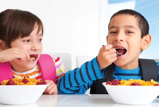 Child with backpack eating from a bowl of cereal and fruit