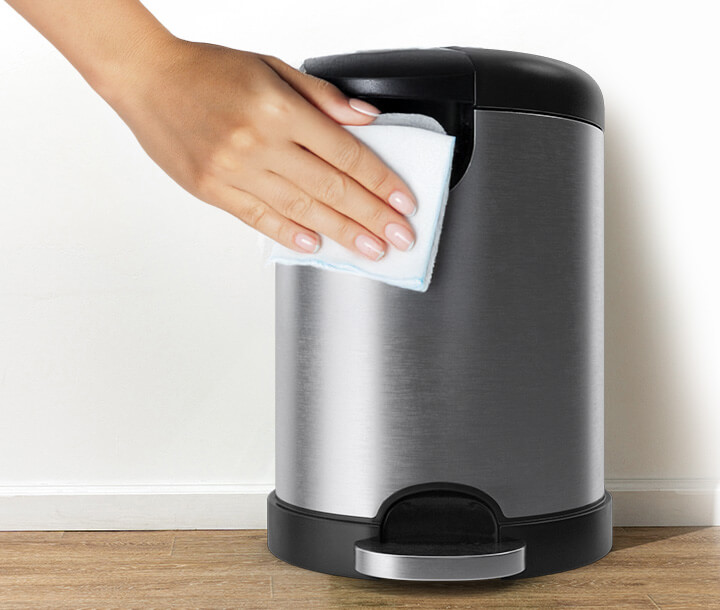 A hand wipes a stainless steel trash can with a cloth.
