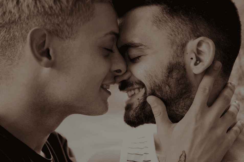 Deux hommes se font face en souriant, prêts à s’embrasser.