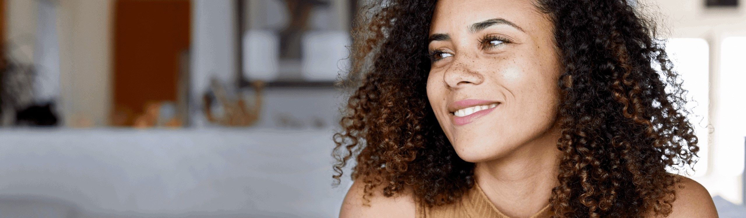 Gros plan d'une femme aux cheveux bouclés souriant et regardant vers sa droite.